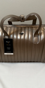 Bronze metallic duffel bag with a visible brand tag on a light background