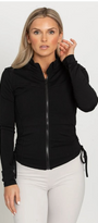 Woman wearing a black jacket and white pants on a plain background