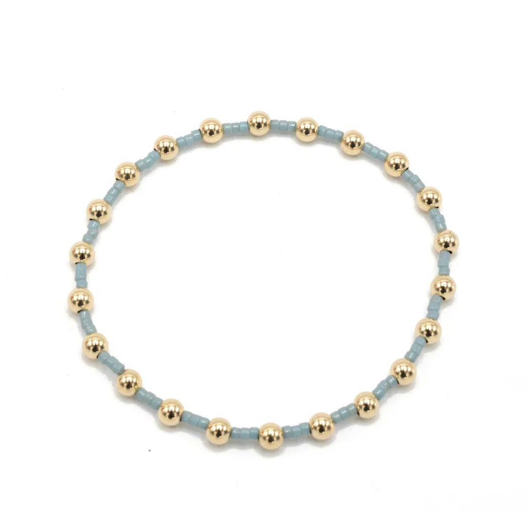 Bracelet with gold beads on a light blue band against a white background