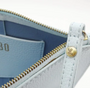 Close-up of a light blue leather wallet with gold zipper and brand logo.
