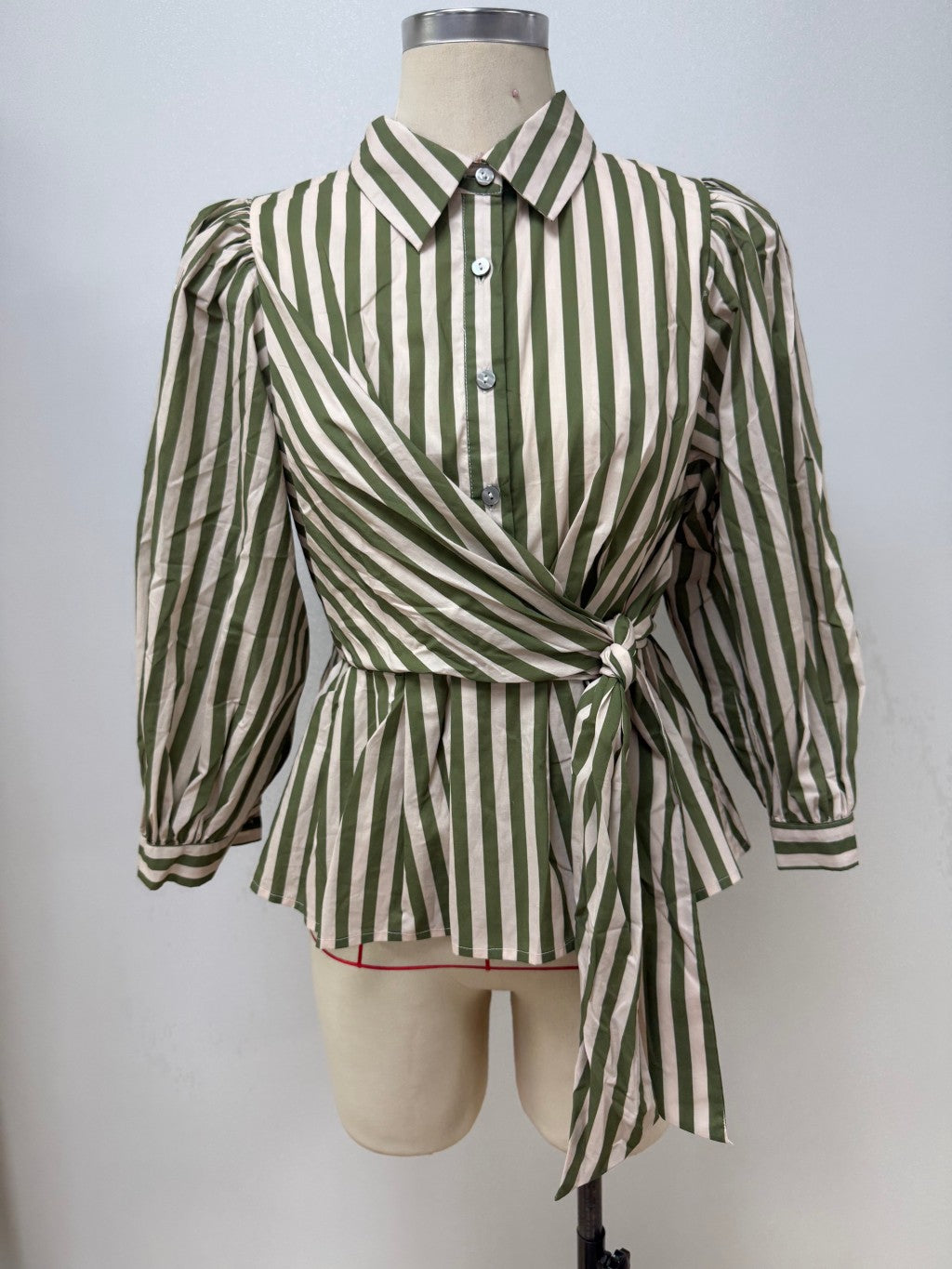 A green and off-white vertically striped wrap blouse with puff sleeves, displayed on a beige mannequin torso against a plain light gray background.
