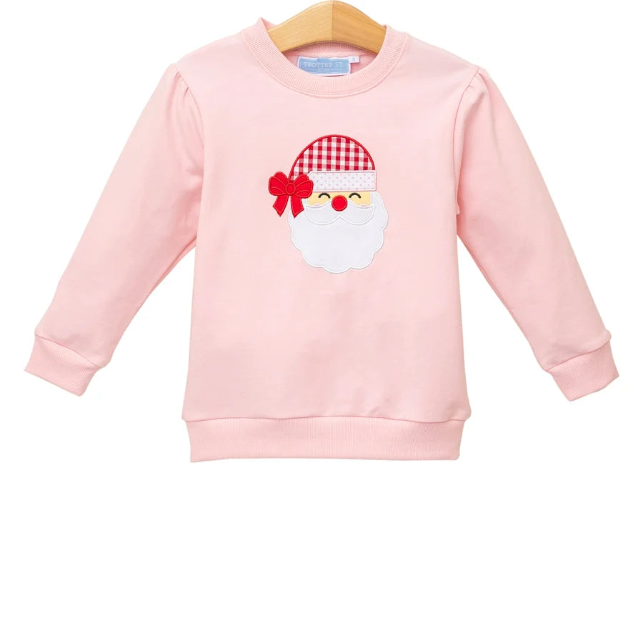 A light pink long-sleeve crewneck sweatshirt for kids, featuring an embroidered Santa Claus face on the front with a red and white checkered hat and red bow.