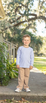 A young boy stands on a concrete walkway outdoors, wearing a light lavender long-sleeve shirt and tan pants.
