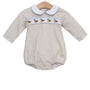 A baby long-sleeve romper in a light beige fabric, featuring a white Peter Pan collar with light blue trim, a horizontal band of embroidered ducks across the chest, and light blue piping along the cuffs and collar, hanging on a wooden hanger against a white background.