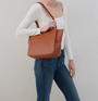 Person holding a brown leather bag against a plain background