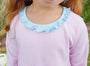 A close-up of a child wearing a pink and white striped long-sleeve top with a light blue ruffled neckline.