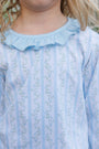 Close-up of a child wearing a light blue long-sleeve top with vertical stripes, a ruffled collar, and a delicate floral print.