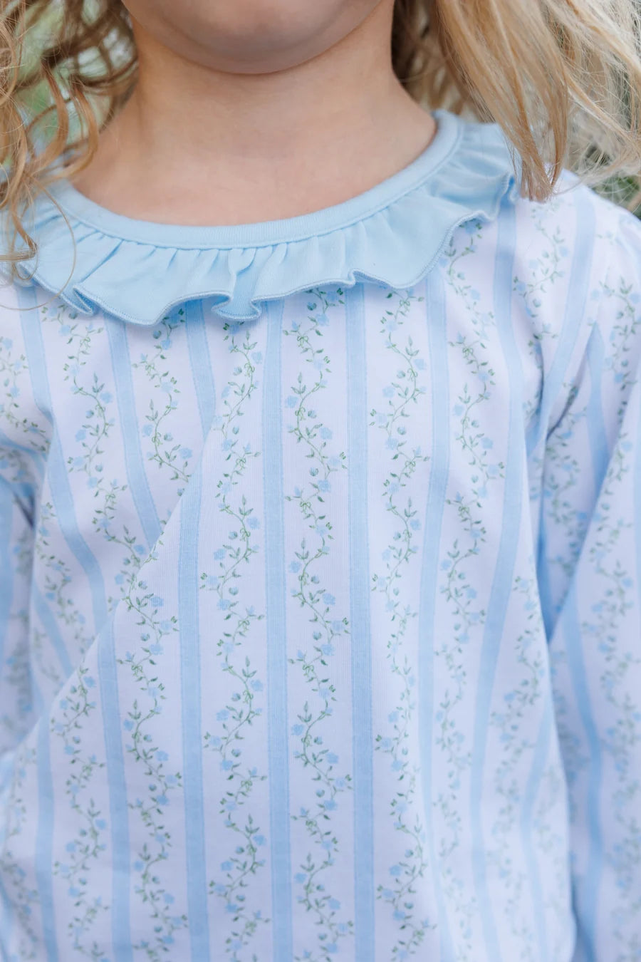 Close-up of a child wearing a light blue long-sleeve top with vertical stripes, a ruffled collar, and a delicate floral print.