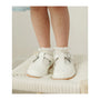White baby shoes with ruffles worn by a child on a soft surface.