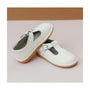 Pair of white children's shoes with a strap on a light pink background