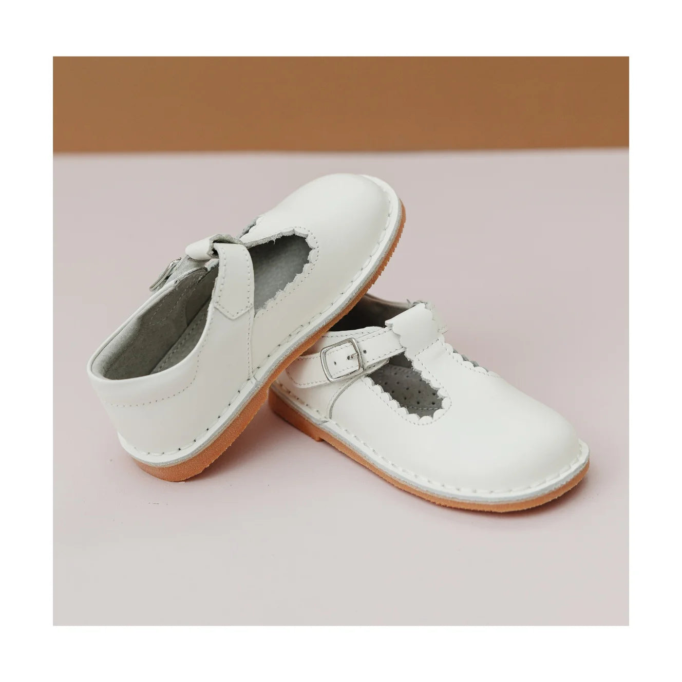 Pair of white children's shoes with a strap on a light pink background