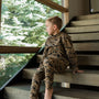 Child in camouflage outfit sitting on a staircase with greenery outside