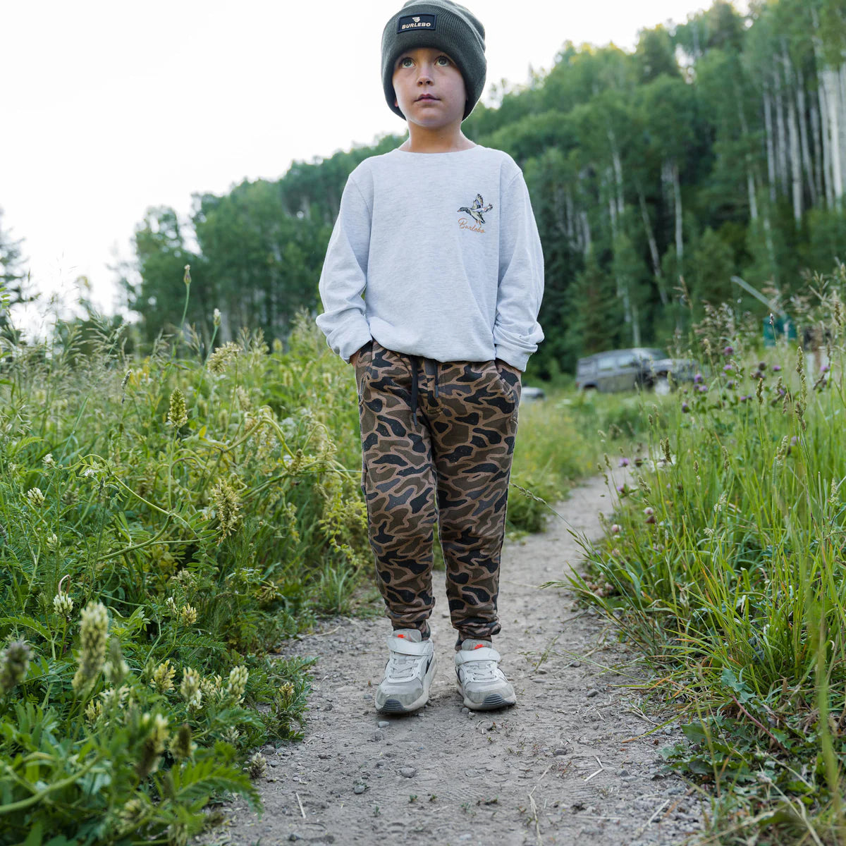 Child standing on a dirt path surrounded by greenery