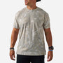 A man wearing a short-sleeve crewneck t-shirt with an abstract camouflage pattern in beige, gray, and white, paired with black pants and accessories.