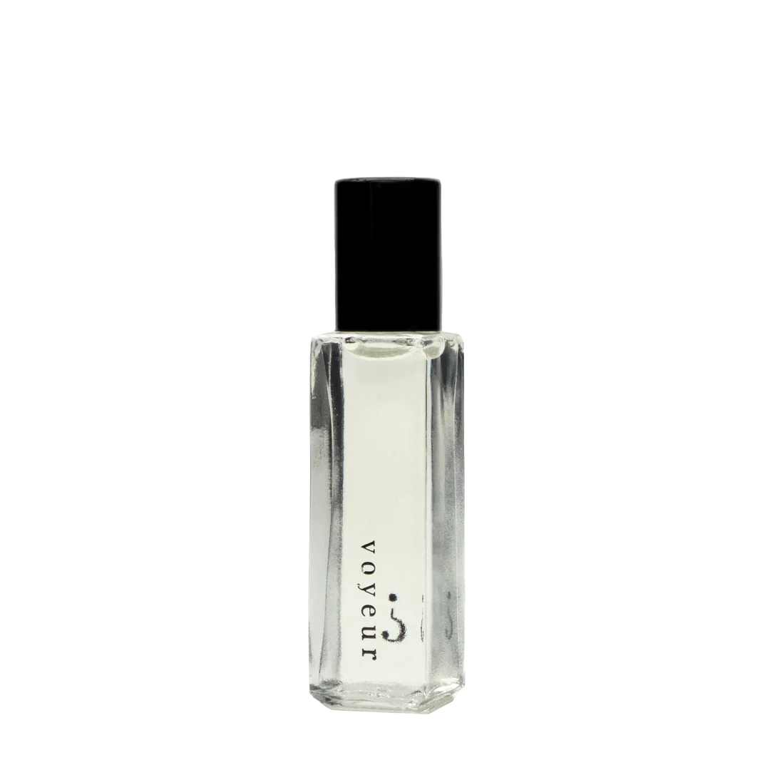 Clear perfume bottle with black cap on a white background, featuring the brand 'voyeur'.