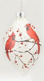 A white Christmas ornament shaped like a teardrop, decorated with two red cardinals perched on branches with small red berries, hanging from a silver cap.