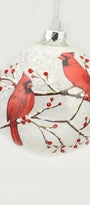 A round clear glass Christmas ornament featuring a printed design of two red cardinals perched on branches with small red berries against a white background.