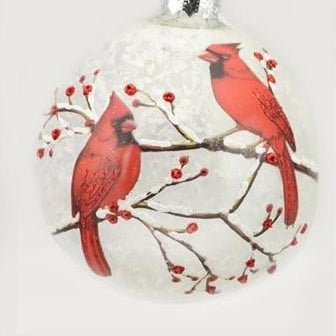 A round clear glass Christmas ornament featuring a printed design of two red cardinals perched on branches with small red berries against a white background.