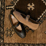 Two Mary Jane style flats, one in dark brown leather and one in tan suede, displayed on a patterned brown rug.