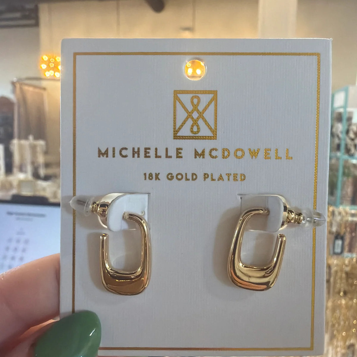 Gold hoop earrings on a Michelle McDowell branded card held by a hand with green nail polish.