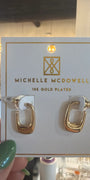 Gold hoop earrings on a Michelle McDowell branded card held by a hand with green nail polish.