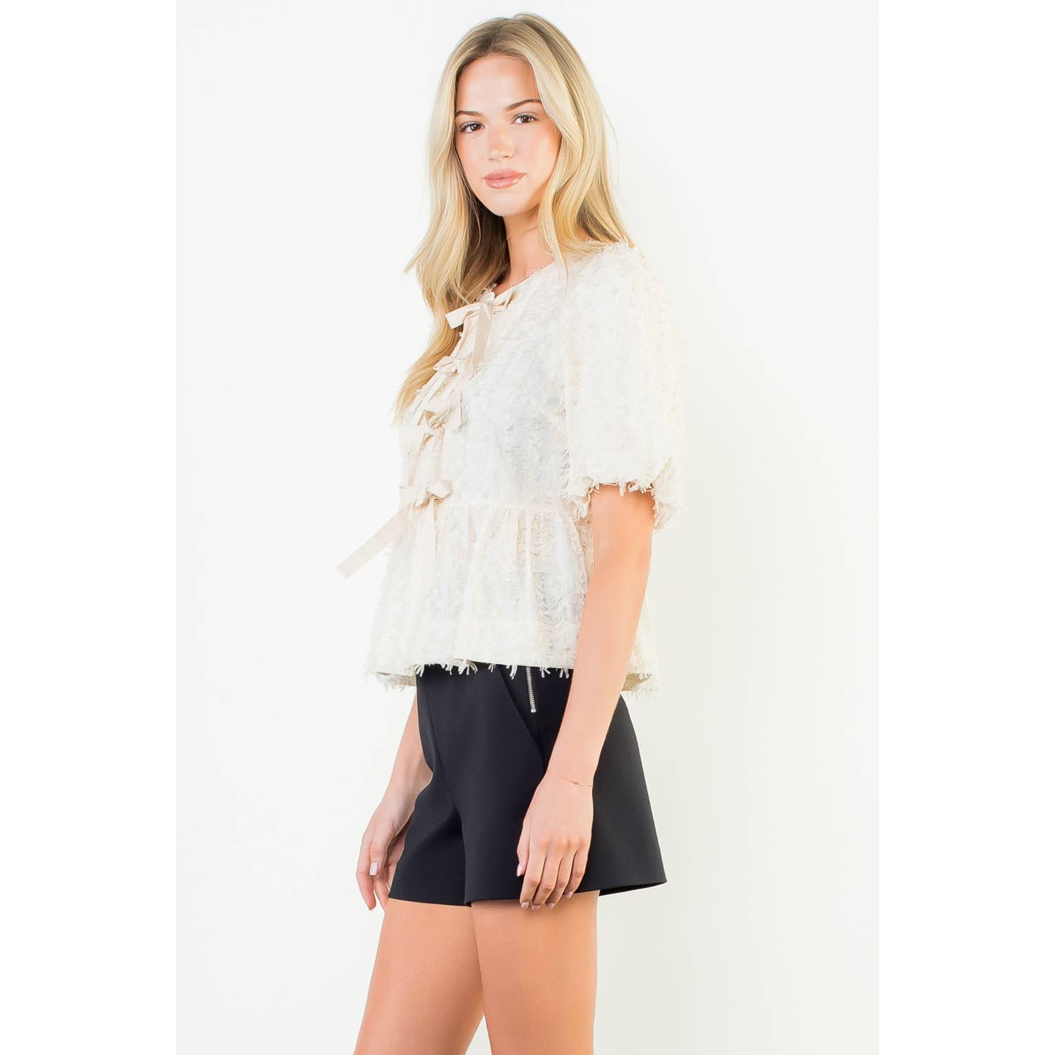 Woman wearing a white lace top and black shorts on a white background