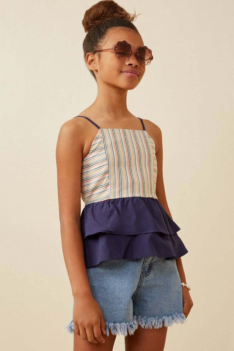 Young girl wearing a striped top and denim shorts against a beige background