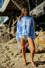 Woman wearing a blue sweatshirt with 'Lake' text on a sandy beach.
