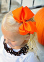Child wearing an orange headband with a large bow, standing outdoors.