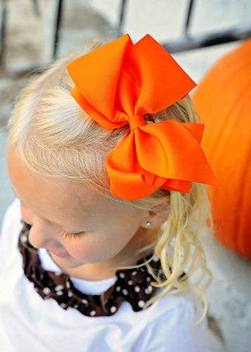 Child wearing an orange headband with a large bow, standing outdoors.