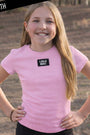 Young girl wearing a pink t-shirt with 'LULU MAC' logo outdoors.