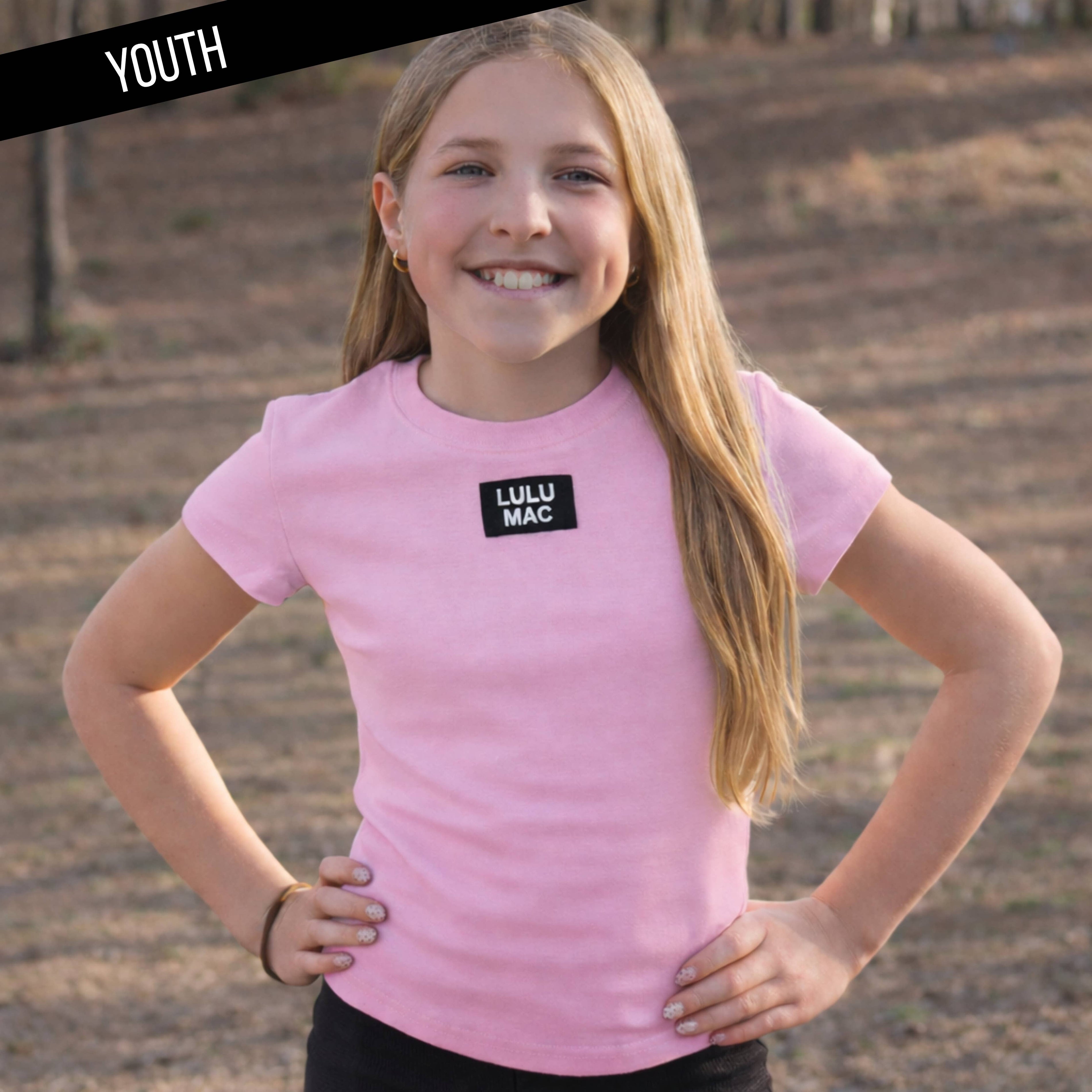 Young girl wearing a pink t-shirt with 'LULU MAC' logo outdoors.