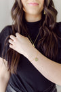 A close-up lifestyle shot of a woman wearing a delicate gold chain necklace and a matching gold bracelet with small circular charms, paired with a black t-shirt.