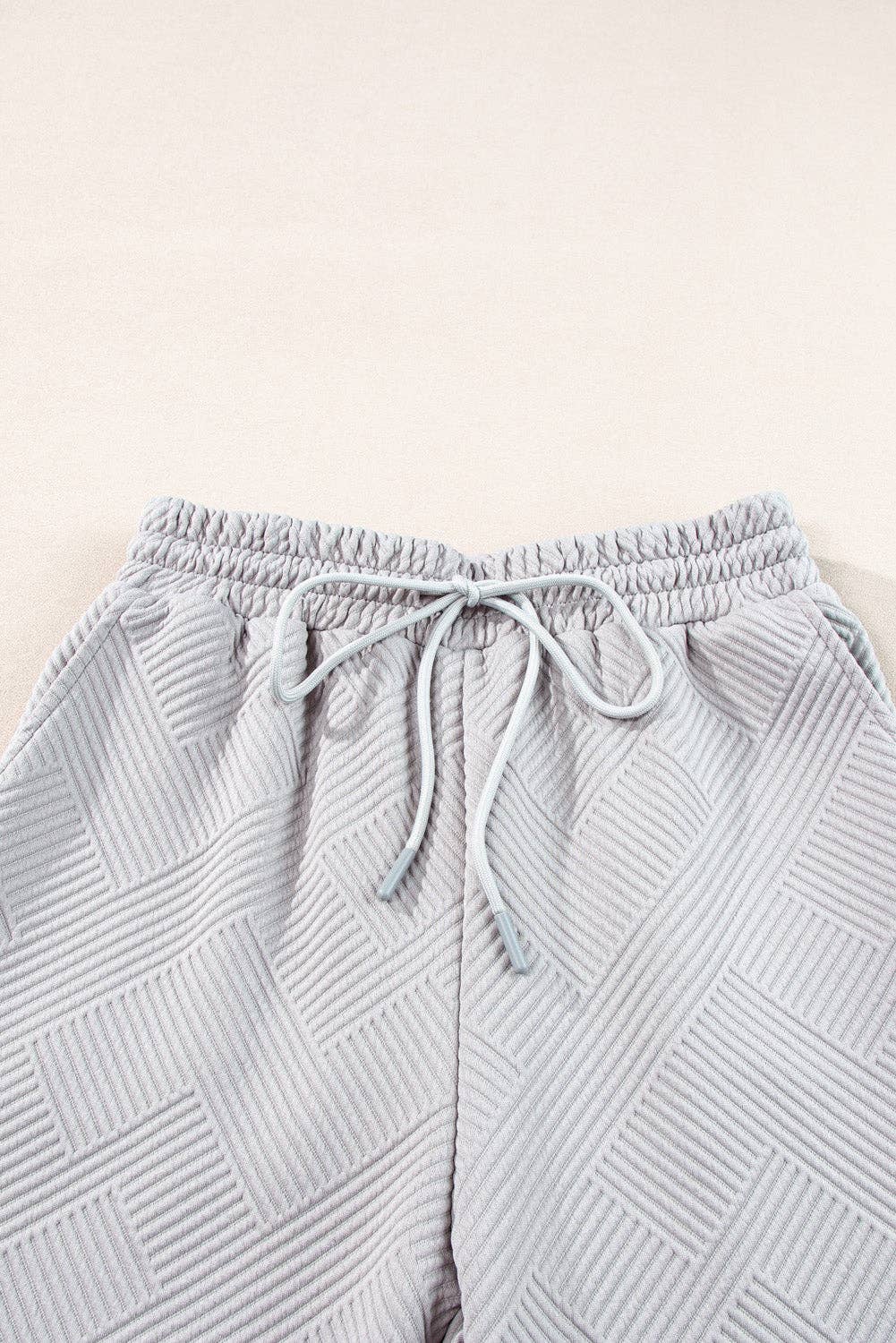 Light gray textured pants with drawstring on a light beige background