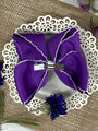 Purple hair bow with a silver clip on a decorative white plate