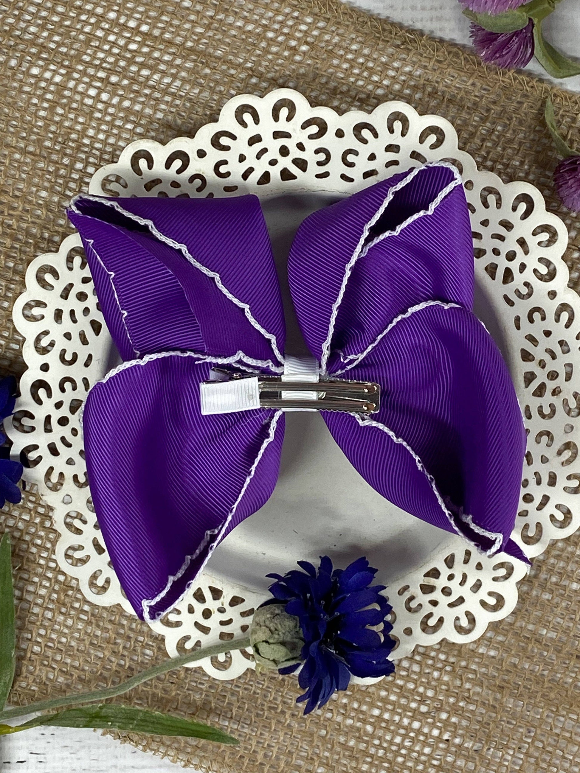Purple hair bow with a silver clip on a decorative white plate