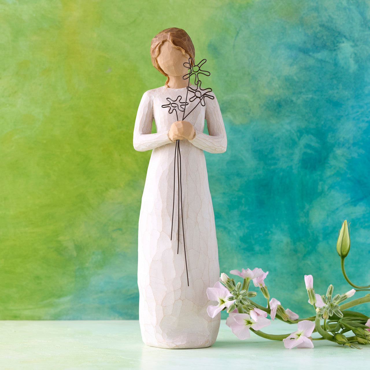 White figurine of a woman holding flowers against a green and blue gradient background