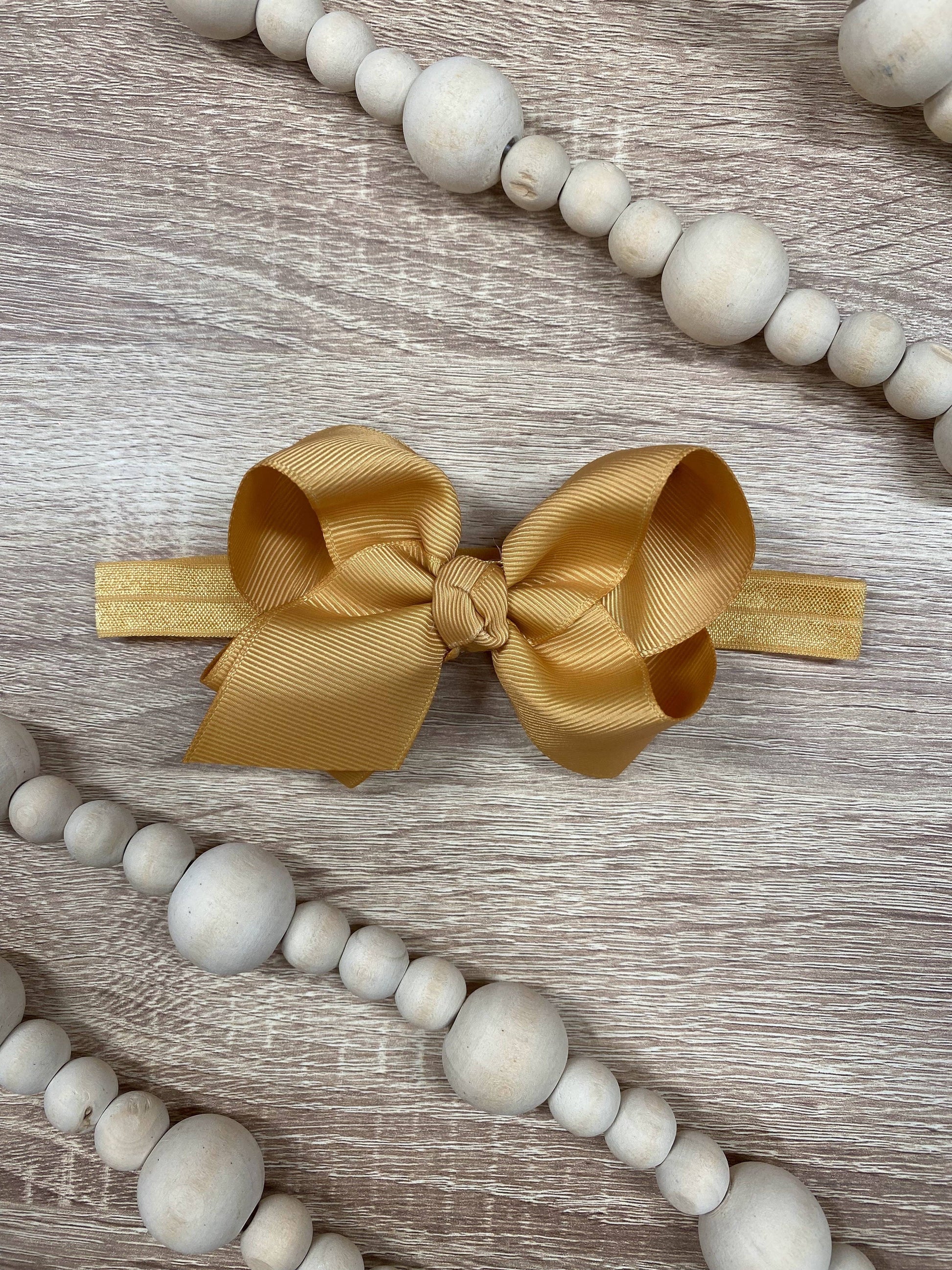 Gold bow headband on a wooden surface with decorative beads