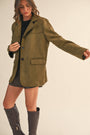 Woman wearing a green coat and gray knee-high boots on a beige background