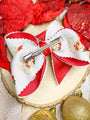 Red and white bow with a hair clip on a wooden surface with Christmas ornaments.