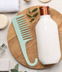 Mint green comb and white bottle on a wooden board with leaves and towels in the background