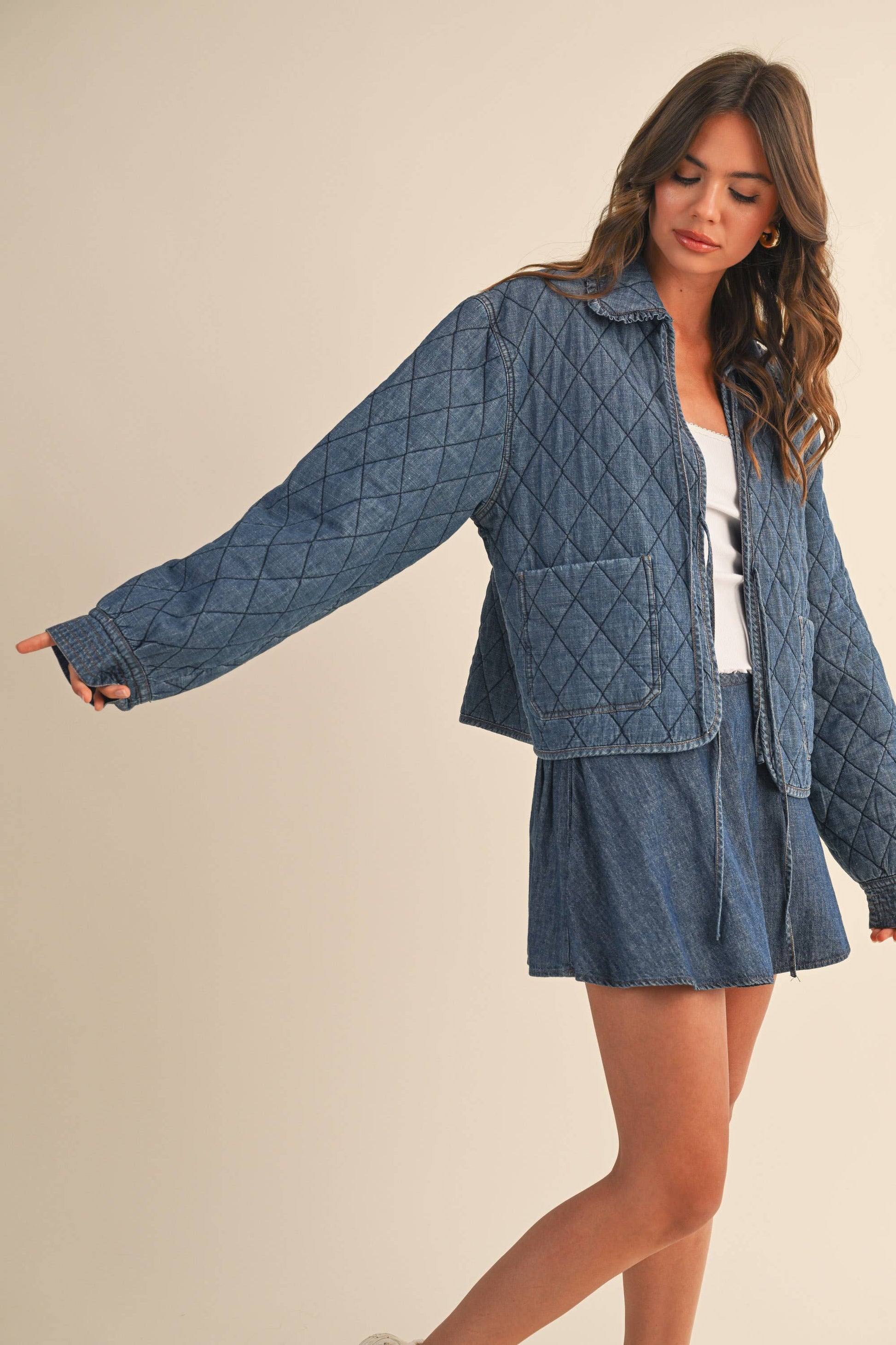 Woman wearing a blue quilted jacket with a skirt against a beige background