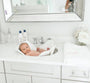 Baby in a white basin with a mirror above in a bathroom setting