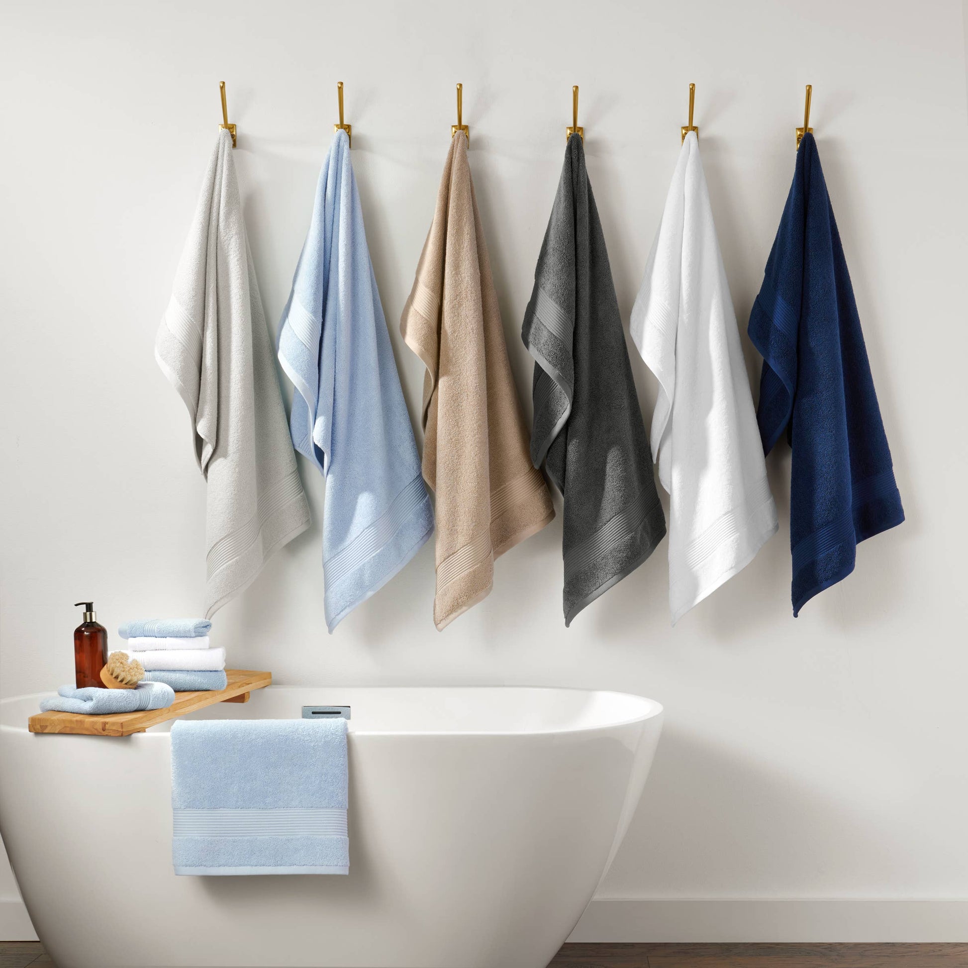 Set of six towels in various colors hanging on hooks above a bathtub.