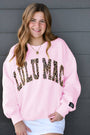 Person wearing a pink sweatshirt with leopard print text against a gray wall.