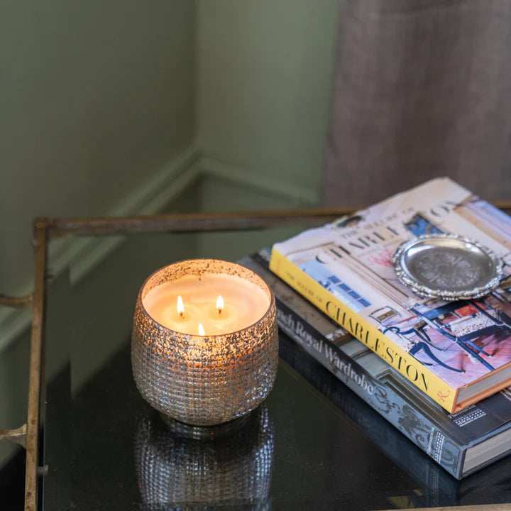 Candle in a decorative holder on a table with books in the background