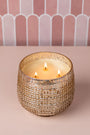 Decorative candle in a textured holder on a pink surface with a striped background