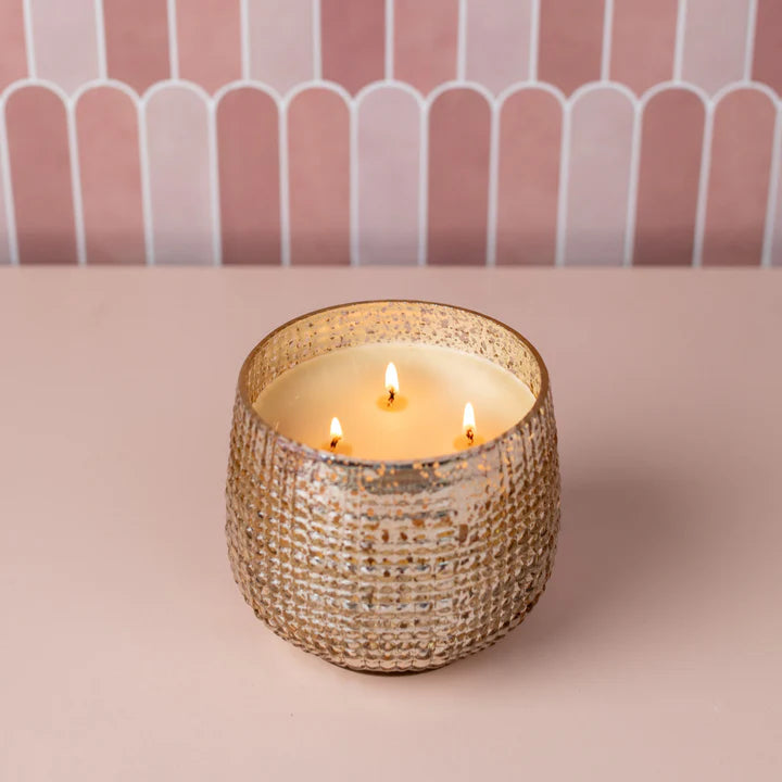 Decorative candle in a textured holder on a pink surface with a striped background