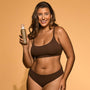 Woman in brown bikini holding a tan-colored bottle against a beige background