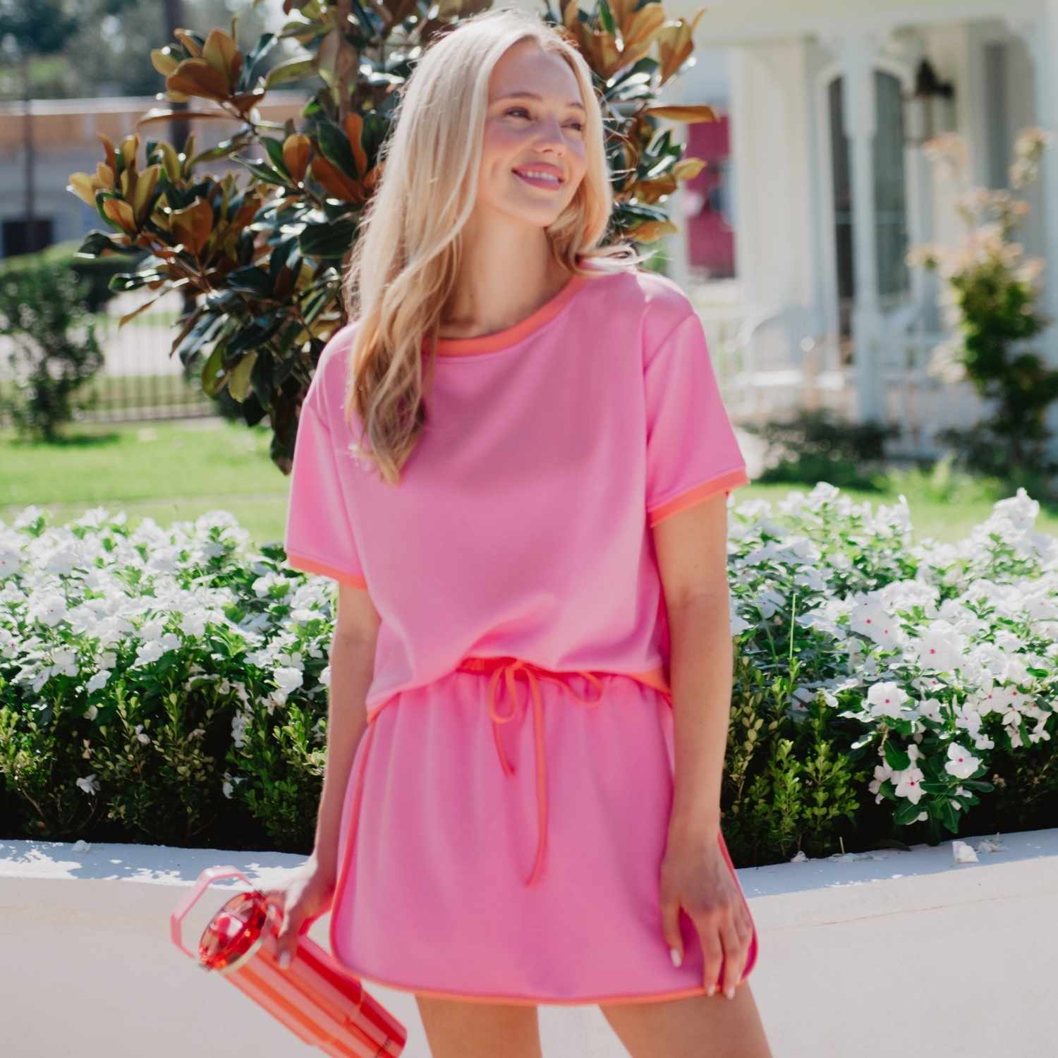 Woman in a pink dress standing outdoors with flowers and a building in the background